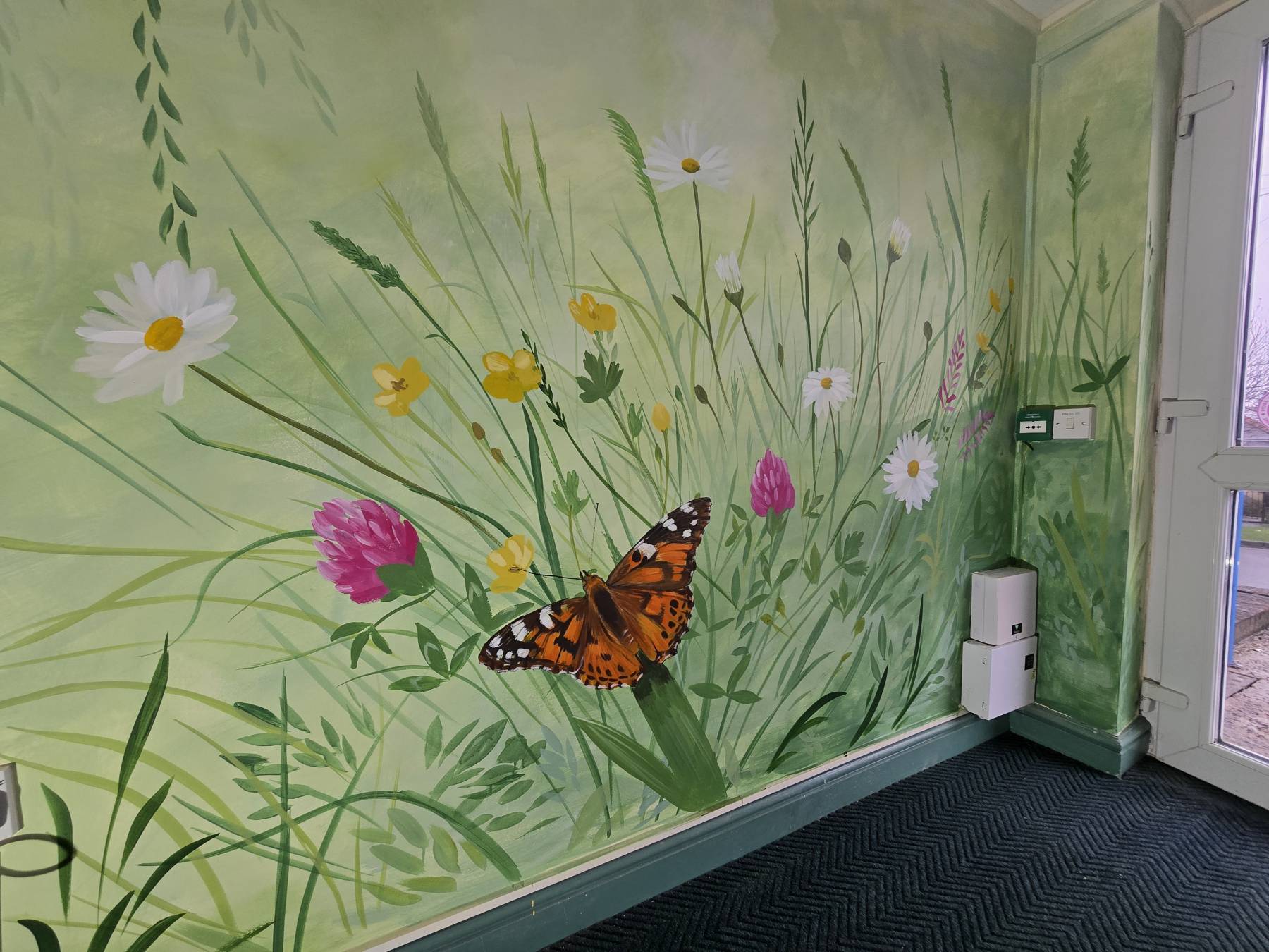 Wildflower meadow mural painted across a foyer corner at a Flying Start centre, with a butterfly resting on a leaf